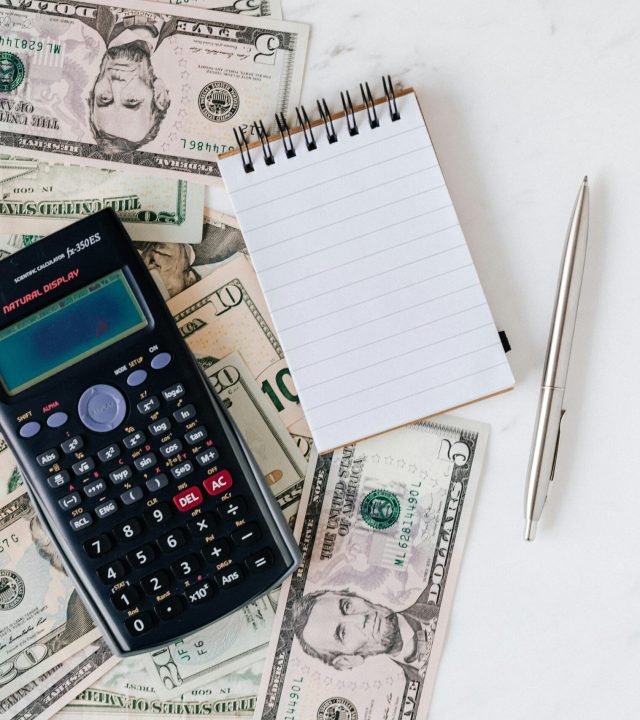 Flat lay of US dollar bills with calculator and notebook for budgeting.